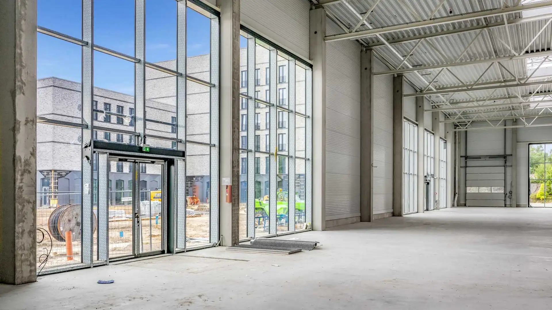 Foto aus der Bauphase des Spurwerkkomplexes. Dargestellt ist eine große Halle mit Glasfront als Eingang und hohen Decken. Außerhalb der Halle sind Baugeräte und weitere Gebäude des Spurwerkkomplexes zu sehen.