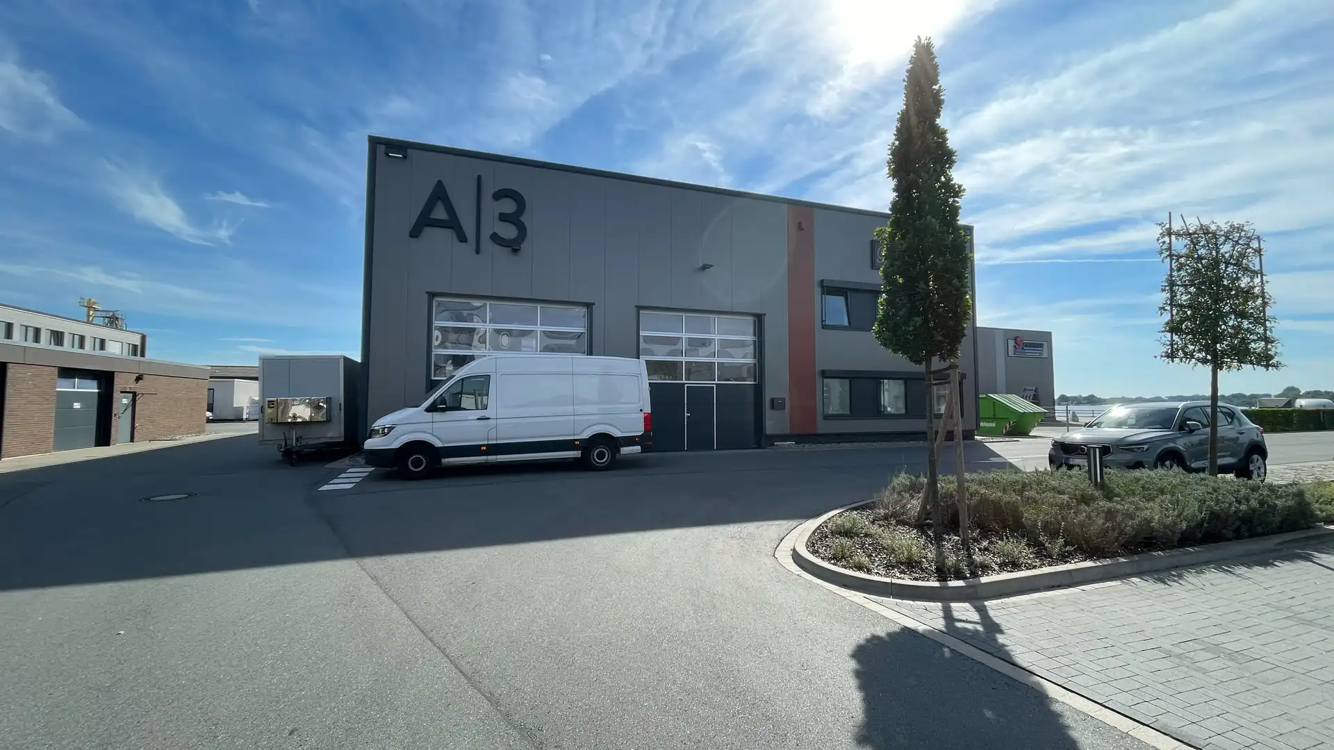 Foto der Halle A3 am Allerkai. Abgebildet ist eine Lagerhalle mit zwei großen Garagen und einem weißen Sprinter davor.